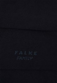 Fekete, puha textúrájú kötött zoknik, az alján világoskék betűkkel "FALKE FAMILY" felirattal.