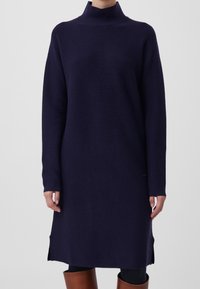 Robe à col roulé bleu marine en tissu tricoté doux, avec manches longues, fentes sur les côtés et coupe décontractée. Finition texturée ajoutant de la profondeur.