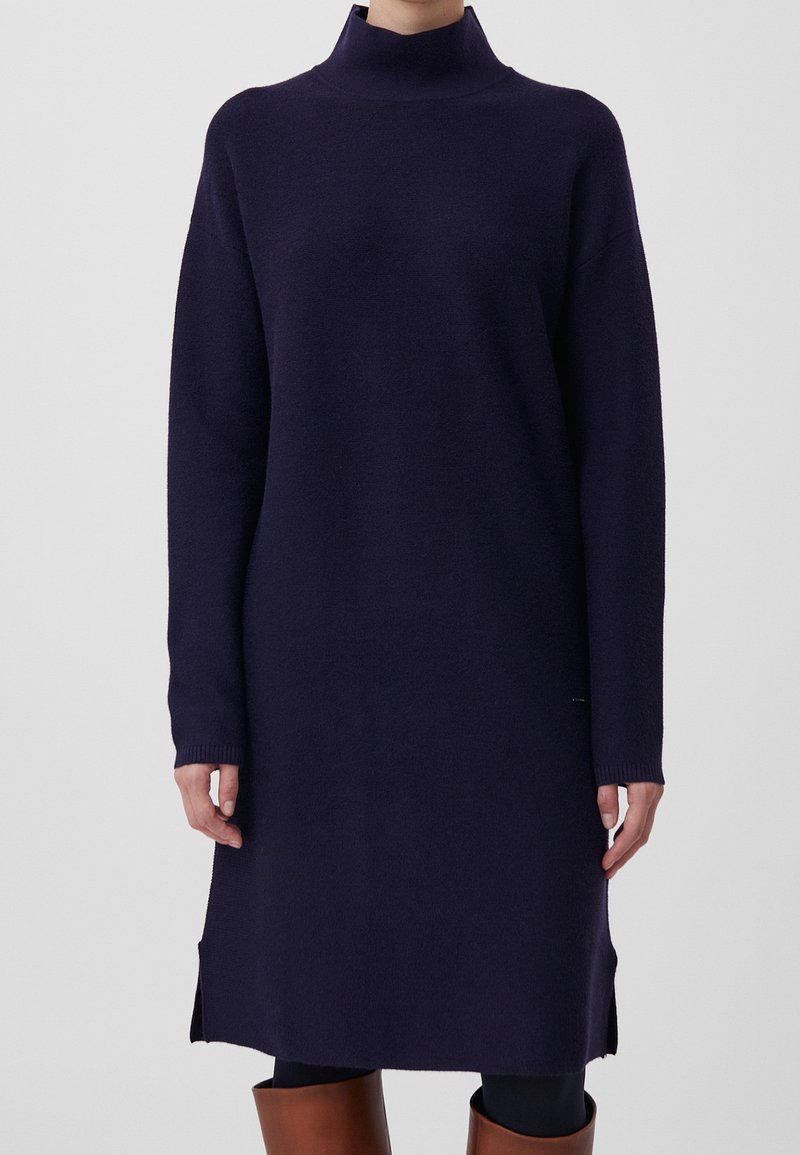 Robe à col roulé bleu marine en tissu tricoté doux, avec manches longues, fentes sur les côtés et coupe décontractée. Finition texturée ajoutant de la profondeur.