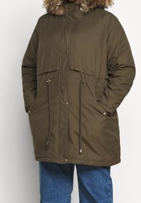 Chaqueta parka acolchada en verde oliva con capucha forrada de piel, cordones ajustables en la cintura y cierre de botón a presión, que presenta bolsillos laterales.