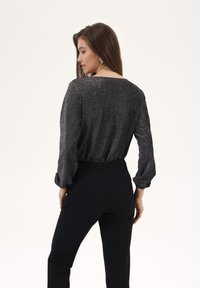 Sorte bukser med en tætsiddende talje, parret med en mørk, tekstureret overdel med lange ærmer og løs pasform. Glitrende detaljer i stoffet.