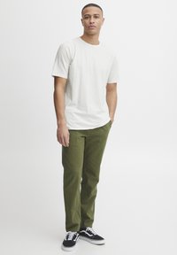 Hvid bomulds t-shirt med korte ærmer, parret med olivengrønne bukser. Sorte og hvide sneakers fuldender outfittet. Simpel, afslappet design.