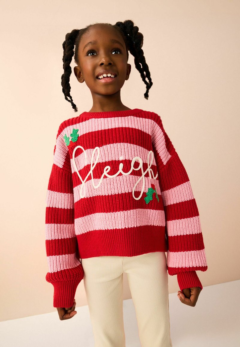 Pull en tricot rouge et rose rayé avec le mot "Sleigh" en blanc, accompagné d'accents de houx vert. Coupe ample et poignets côtelés.
