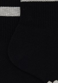 Calzini neri con due strisce orizzontali grigie. Realizzati in un tessuto morbido con una texture a coste e zone del tallone e della punta rinforzate.