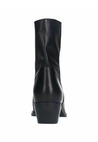 Bottine en cuir noir avec une forme légèrement effilée, un petit talon carré et une texture lisse, présentant des coutures minimales et sans ornements.