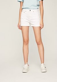 Vita denimshorts med uppvikta fållar, med fem fickor och metallknäppning, kombinerade med en ljusblå t-shirt och vita sneakers.