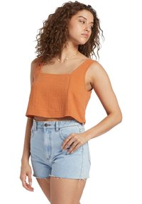 Cropped orange top with textured fabric, square neckline, and wide straps. Paired with high-waisted light blue denim shorts featuring frayed hems.