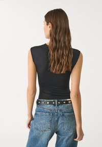 Black sleeveless bodysuit with a fitted design, paired with high-waisted blue denim jeans featuring a studded black belt.