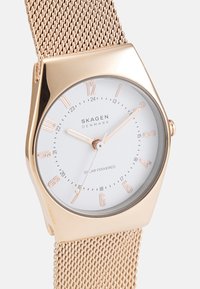 Gold-tone mesh-band solar-powered watch with a round white dial, rose gold hour markers, and a minimalist design.