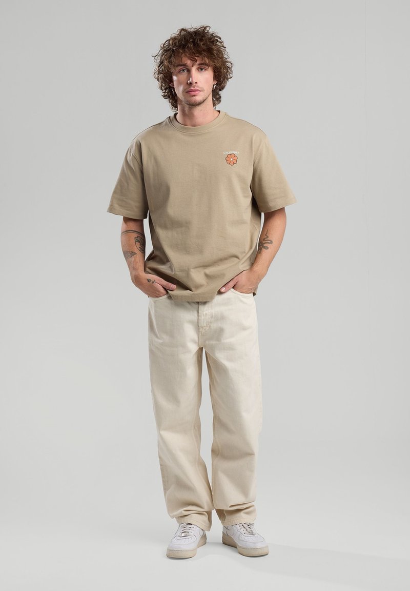 Beige puuvillane T-särk lühikeste varrukatega, millel on väike oranž lillemuster. Kombineeritud heledates beežides laiad püksid ja valged tennisetossud.