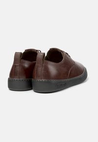 Chaussures en cuir marron avec une texture lisse et un design minimaliste. Elles présentent une semelle en caoutchouc noir et un détail de couture le long du bord.