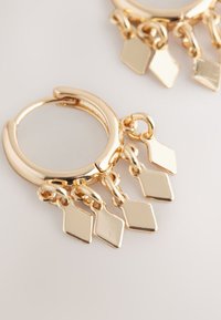 Goldene Creolen-Ohrringe mit drei hängenden, diamantförmigen Anhängern, mit glänzendem Finish und glatter, polierter Oberfläche.