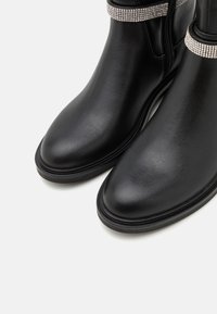 Bottines en cuir noir avec bouts ronds, semelles basses, fermetures éclair latérales et brides ornées de strass autour des bords supérieurs.