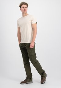Beige t-skjorte med rund hals, olivengrønne cargo-bukser med sidelommer, og brune joggesko med grønne accenter. Enkel og funksjonell design.