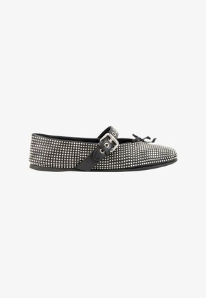 Chaussure plate noire recouverte de petits clous argentés avec une bride noire à boucle et un nœud décoratif à l'avant.