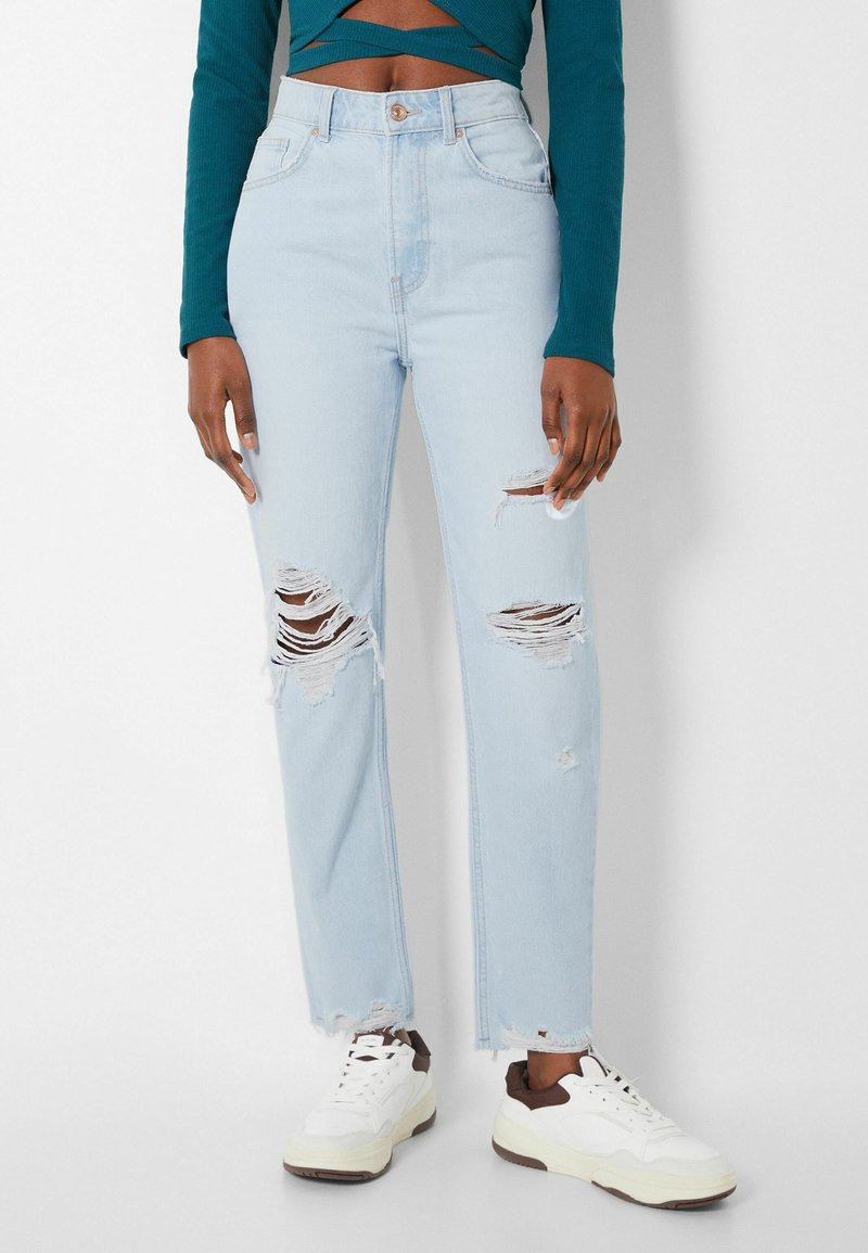 Vaaleansiniset revityt farkut, joissa on hapsuhelmat ja useita kuluneita paikkaajia. Yhdistettyinä valkoisiin ja ruskeisiin tennarit.