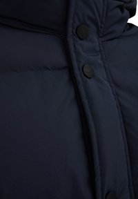 Navy puffer jacket featuring a quilted design, soft texture, and black snap buttons along the front for closure.