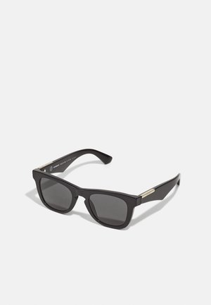Gafas de sol negras con un acabado mate, lentes rectangulares y detalles en tono dorado en las patillas, con un diseño sólido y lentes oscuros.