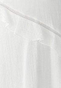 Weißer Stoff mit einer strukturierten, zerknitterten Oberfläche. Verfügt über einen gewellten Rand und einen dünnen gestreiften Akzent entlang der Naht. Weiches, leichtes Material.