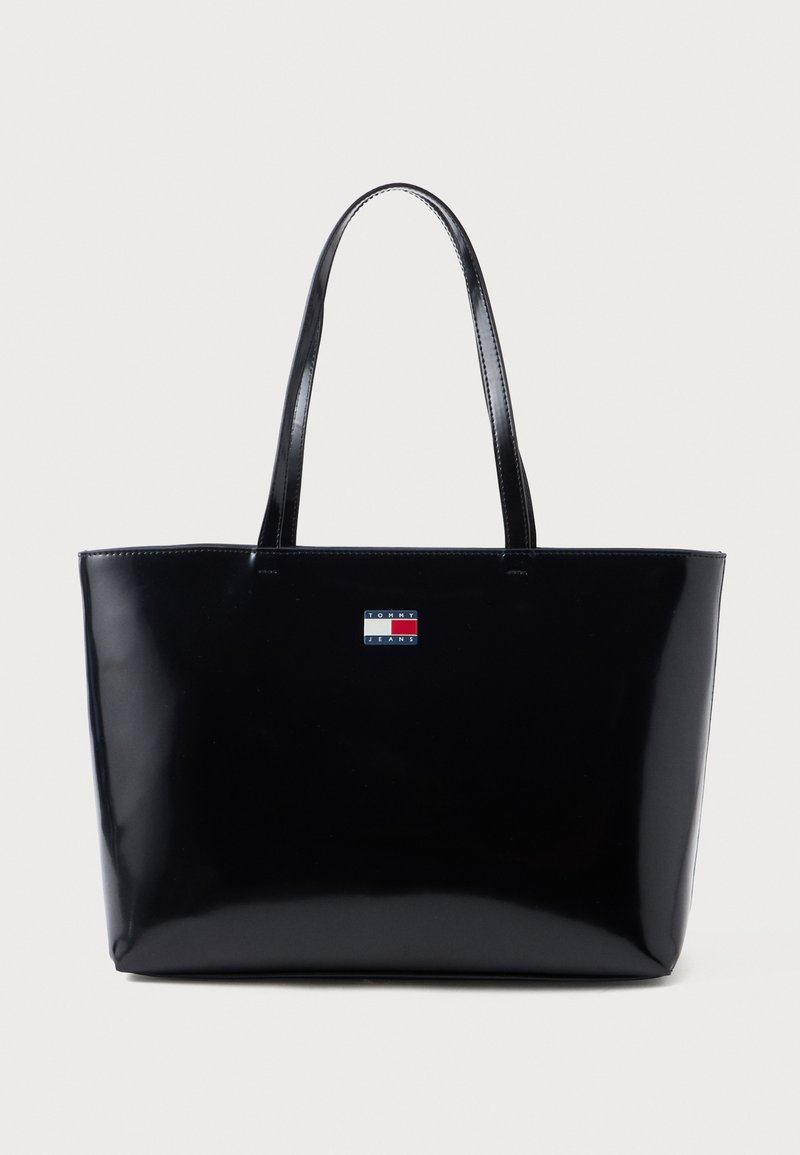 Fekete fényes vászontáska két fogóval. Téglalap alakú, az elején kis logóval, amely piros, fehér és kék színekben pompázik.