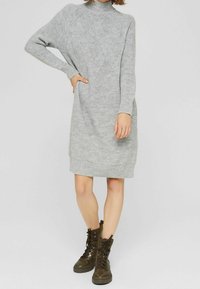 Robe grise tricotée avec un col montant, des manches longues et un motif en losanges texturé, associée à des bottines vertes à lacets.