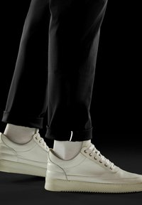Baskets en cuir blanc avec une surface texturée, bout rond et semelle en caoutchouc épaisse. Un pantalon noir avec des revers réfléchissants.