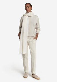 Lys beige sweater, creme tørklæde, elfenbensfarvede bukser og beige sneakers. Bløde teksturer, afslappet pasform og afslappet design med ribbede detaljer.