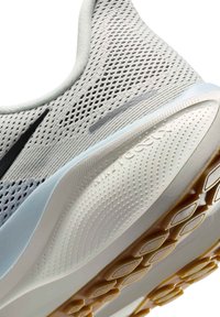 Gros plan d'une chaussure de sport en mesh blanc et gris avec un logo noir, une semelle amortie et une semelle extérieure texturée avec des crampons hexagonaux en caoutchouc.