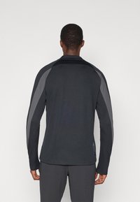 Tricou sportiv negru cu mâneci lungi, cu accente gri pe umeri. Dispune de un guler și are o croială normală, fabricat dintr-un material neted și respirabil.