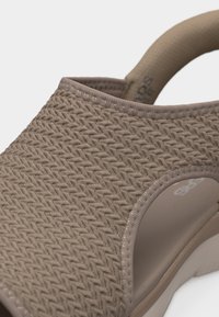 Κοντινή εικόνα της μπεζ υφασμάτινης επιφάνειας πάνω μέρους ενός σανδαλιού με ένα άνοιγμα κοντά στην άκρη της σόλας.