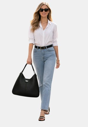 Donna con occhiali da sole, camicia bianca, jeans azzurri chiari, cintura nera e sandali, che porta una grande borsa nera mentre cammina.