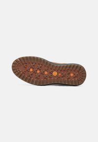 Gumowa podeszwa o wytrzymałej konstrukcji, z głębokim bieżnikiem i teksturowaną powierzchnią. Kolor brązowy z czarnymi akcentami. Widoczna logo Timberland.