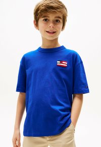 Königsblaues Baumwoll-T-Shirt mit kurzen Ärmeln, das auf der Brust mit einem strukturierten Patch in Rot, Weiß und Schwarz versehen ist.