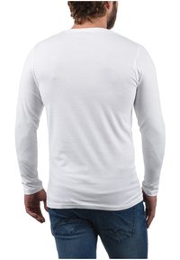 Camisa blanca de manga larga hecha de algodón, con un escote redondeado y silueta ajustada, combinada con jeans de mezclilla azul.