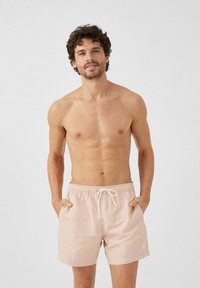 Pantaloni da bagno rosa chiaro con vita elastica e lacci. Presentano tasche laterali e un accento con logo sulla coscia. Tessuto dal tocco morbido.