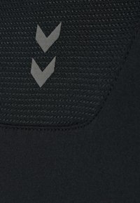 Två ljusgrå nedåtriktade chevronsymboler på texturerad svart tyg med slät svart tyg nedanför.