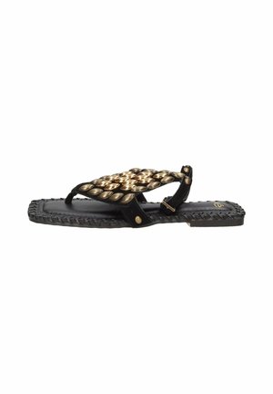 Sandalo nero flat con borchie ovali dorate, suola con bordo intrecciato e fibbia regolabile alla caviglia, mostrato di profilo.