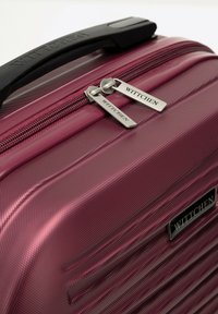 Valigia rigida di colore rosa scuro con una finitura texture, dotata di un manico nero e di cursori metallici con branding.