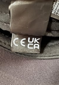 Étiquette de vêtement montrant les marquages de conformité réglementaire CE et UKCA sur un tissu noir à l'intérieur d'un vêtement.