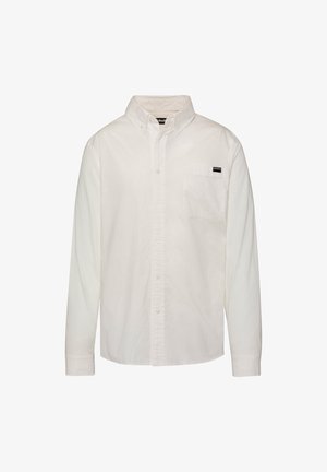 Chemise blanche à manches longues avec col boutonné et poche poitrine affichant une petite étiquette noire et blanche.