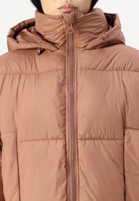 Brun puffjakke med høy krage, glidelås og hette. Materialet er glatt med horisontale sømmer og en lett skinnende overflate.