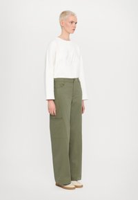 Chemise blanche à manches longues avec logo en relief associée à un pantalon large taille haute vert olive avec poches et fermeture à bouton.