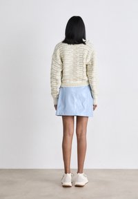 Maglione lavorato a maglia crema con motivo testurizzato, gonna corta in pelle blu e sneakers bianche. Sfondo semplice, con attenzione ai dettagli dell'abbigliamento.