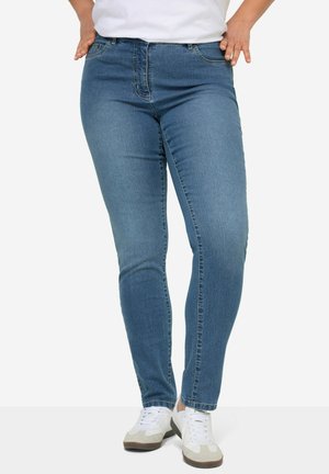 Slim-fit blauwe denim jeans met een klassieke vijf-pockets ontwerp, knoopsluiting en subtiele vervaging. Gepaard met witte sneakers.