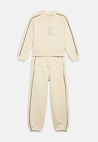 Creme sweatshirt en joggers set, met zwarte zijstrepen en een tonale geborduurde logo op de borst. Zacht materiaal met elastische boorden.