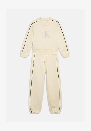 Krém színű pulóver és melegítőnadrág szett, fekete oldalsávokkal és tonális hímzett logóval a mellkason. Puha anyag, rugalmas mandzsettákkal.