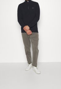 Navy zip-up sweater with a high collar, paired with light gray corduroy pants and white sneakers, featuring a subtle logo on the chest.