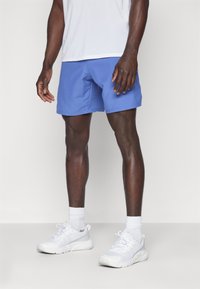 Blaue Sportshorts mit einer glatten Textur und einem elastischen Bund. Getragen mit weißen Turnschuhen und Kniestrümpfen.