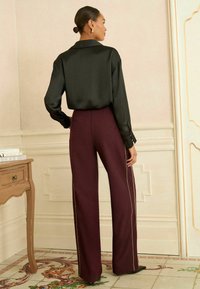 Svart satin långärmad skjorta i kombination med högmidjade bordeauxfärgade byxor med guldiga sidostråk och en avslappnad passform.