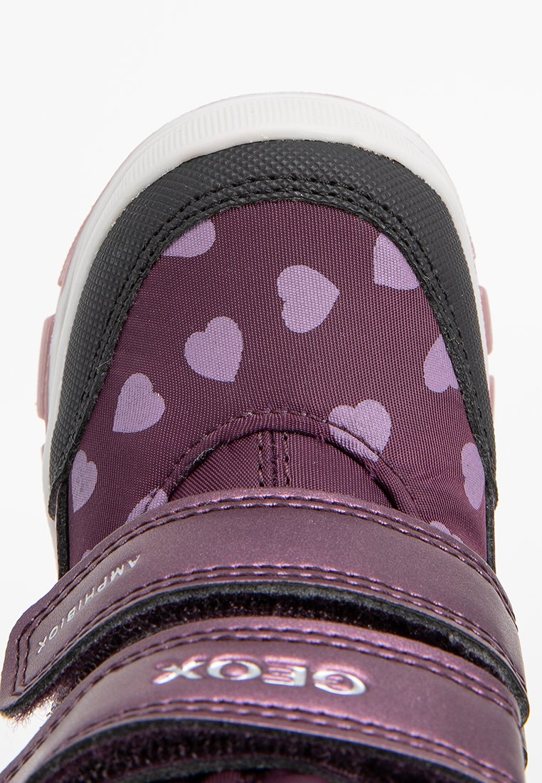 Lila Sneaker mit einem Herzmuster; Obermaterial aus Stoff, schwarze Akzente, weiße Sohle und zwei verstellbare Klettverschlüsse. Verstärktes Zehen-Design.